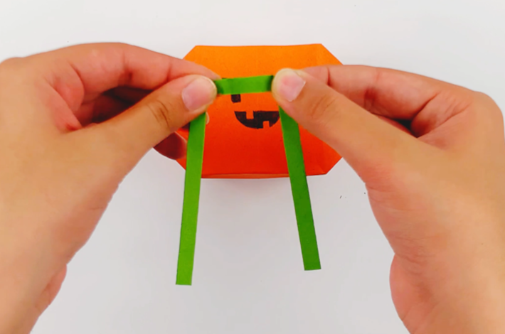 Two hands folding the green paper over to make a handle for the gift bag. 