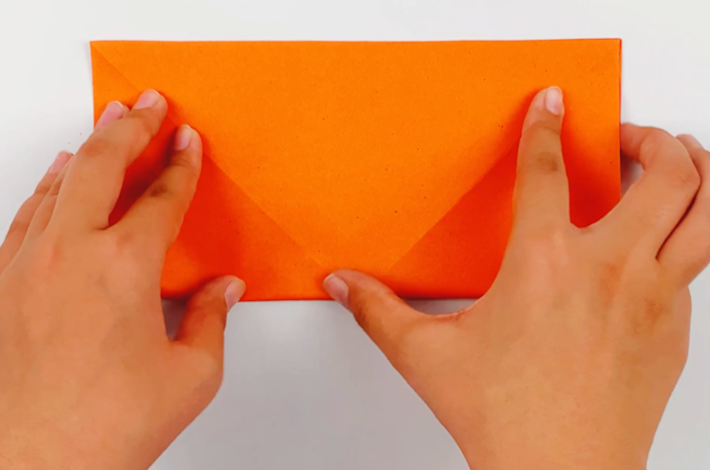 Two hands unfolding the paper and then folding it in half to form a rectangle. 
