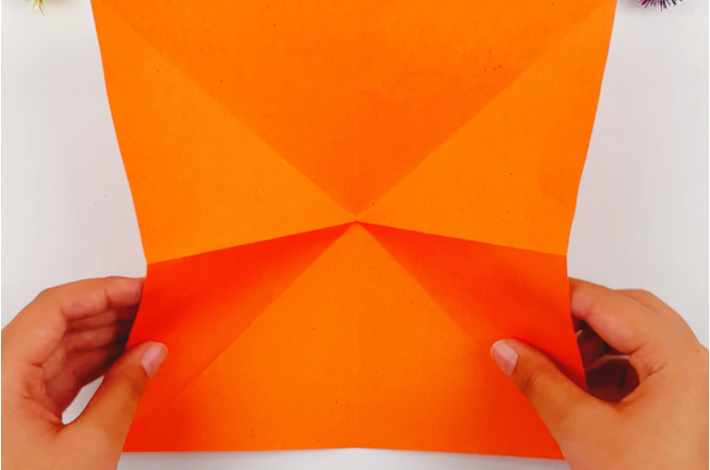 Two hands unfolding the paper to show where the fold lines are. 