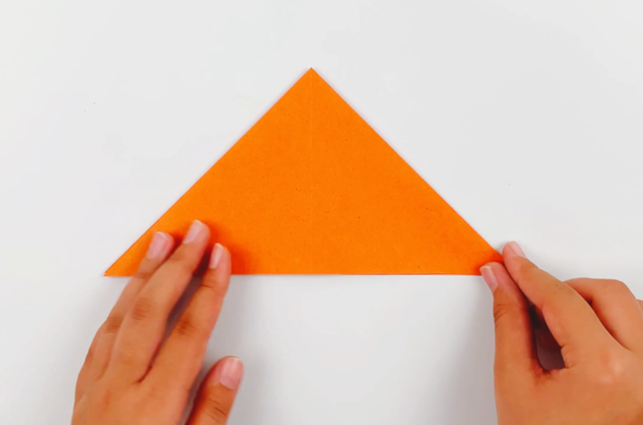 Two hands flattening the top section of the paper towards the bottom to form a triangle. 
