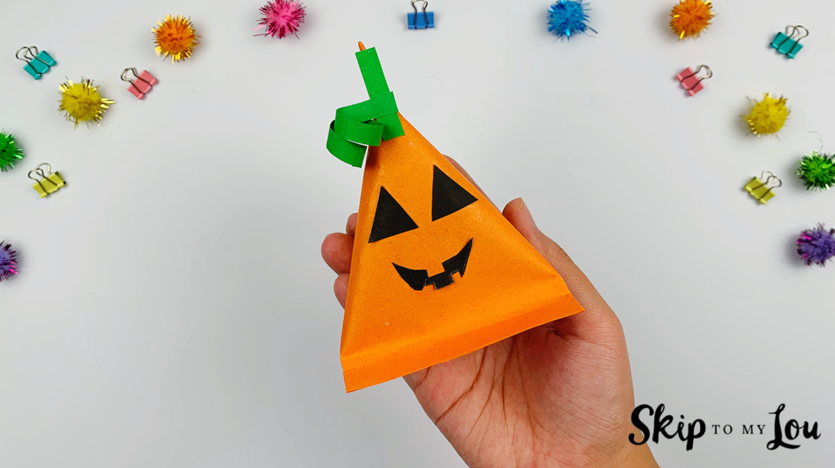 A hand holding a finished paper pumpkin treats bag.