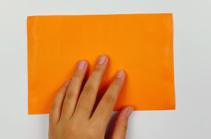A hand holding an organge piece of paper.