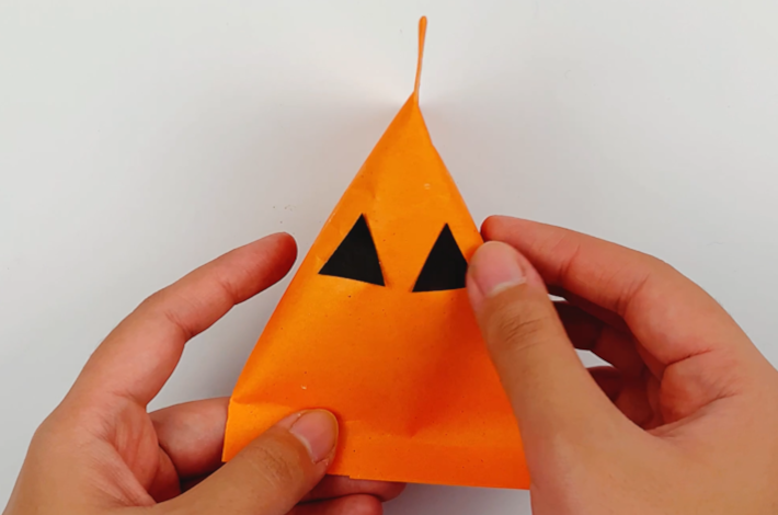 Two hands applying the pumpkins eyes cut out from a black piece of paper.