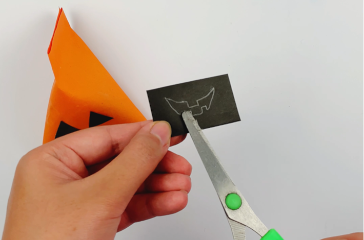 Using a pair of scissors to cut out the pumpkins mouth from a black piece of paper.