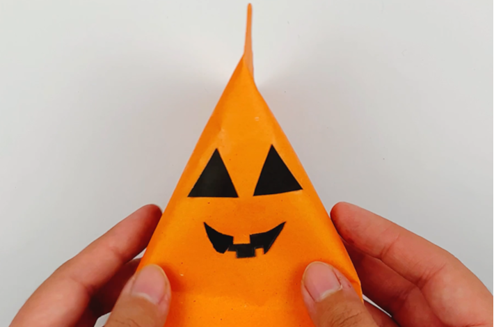 Two hands holding the pumpkin with its eyes and mouth applied.