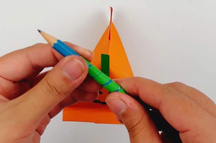 Two hands wrapping a longer strip of green paper around a pencil to curl it.