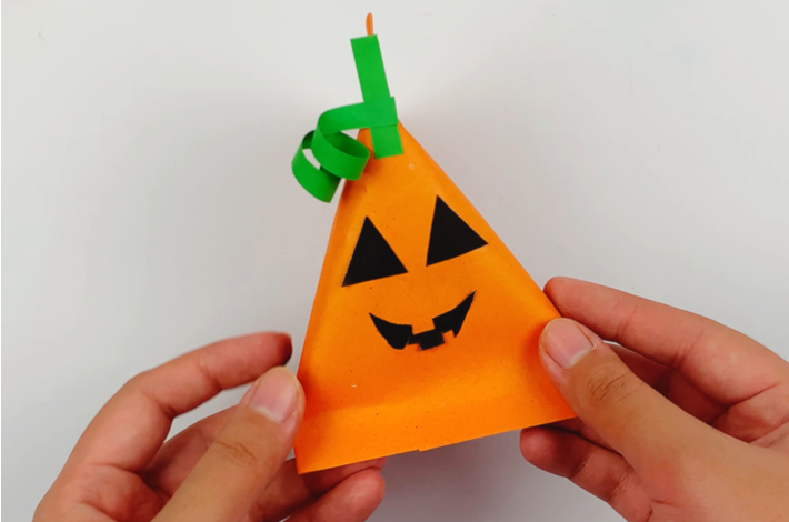 Two hands holding the finished pumpkin treat container.