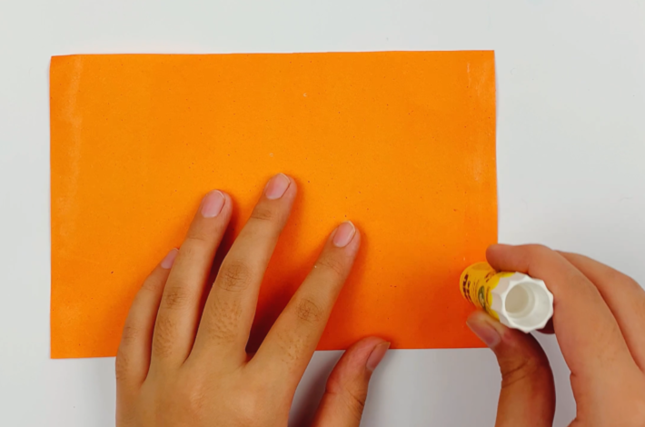 Two hands applying some glue to the outer right edge of the paper.