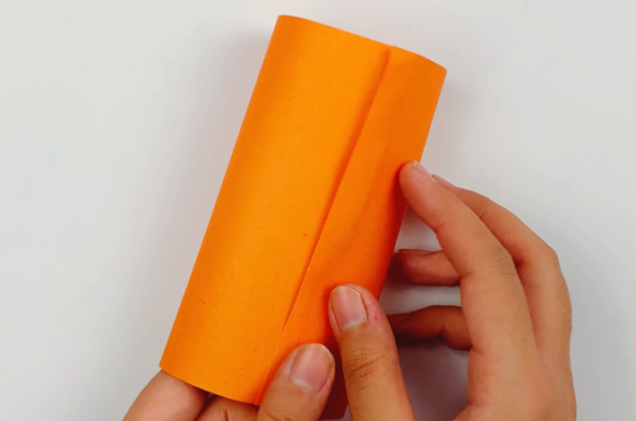 Two hands forming the paper into a cylinder shape and sticking the two ends together.