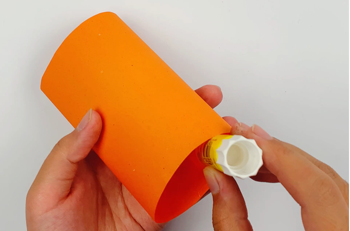 Two hands adding glue to the bottom of the paper inside the cylinder.