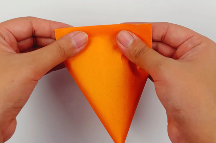 Two hands closing the top of the paper after applying glue.