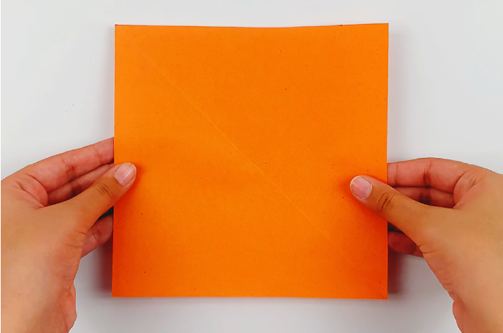 Two hands holding a square  piece of organge paper.