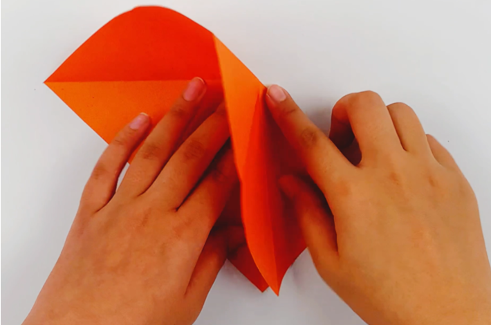 Two hands folding the flaps of the paper inwards and down. 