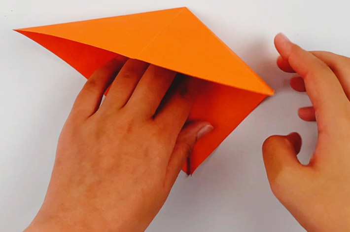Two hands folding the flaps of the paper inwards and down. 