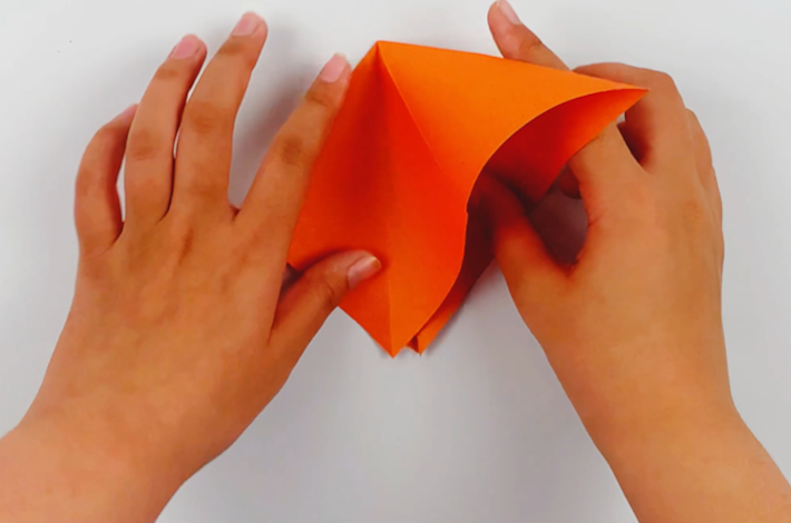 Two hands forming the paper into a diamond shape. 
