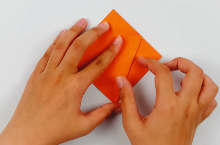 Two hands folding the top flap on the right hand side to the center. 
