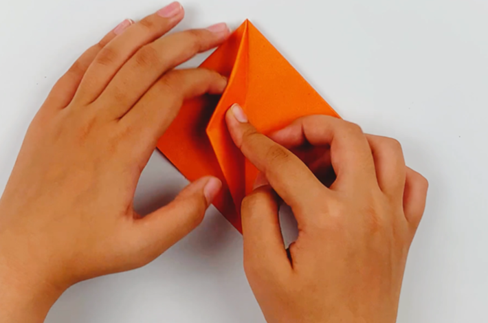 Two hands takign the folds made on the right top flap over to the left-hand side. 