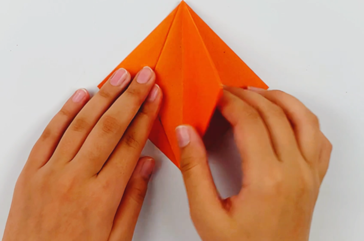 Two hands folding the next flap on the right over to the left.