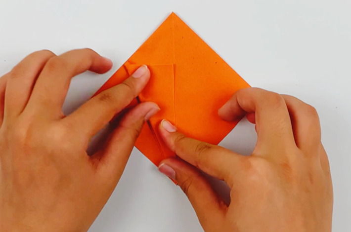 Two hands folding the top flap on the left hand side to the center. 