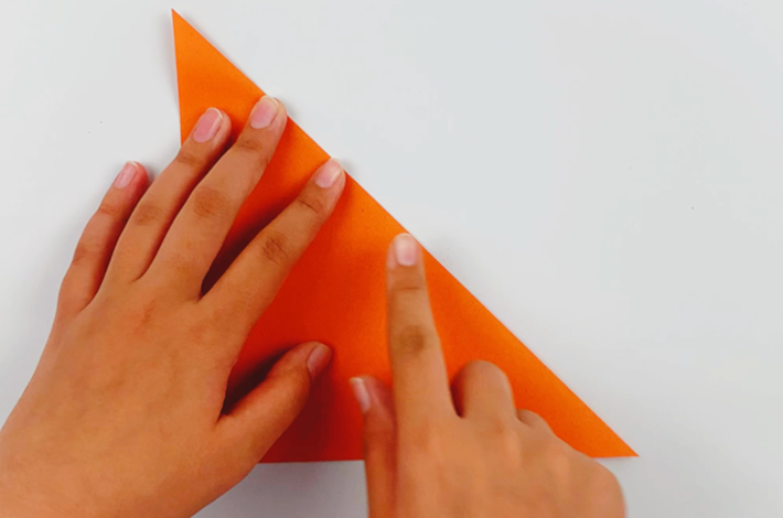 Two hands folding the top right hand corner of the paper downwards to form a triangle. 