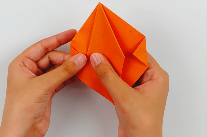 Two hands folding the left and right hand corners of the outer diamond inwards. 