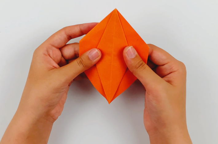 Two hands holding the orange paper with the folds showing upwards and the corners tucked inside. 