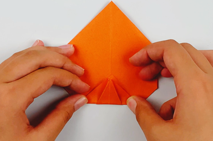 Two hands folding the bottom section over once the paper has been flipped over. 