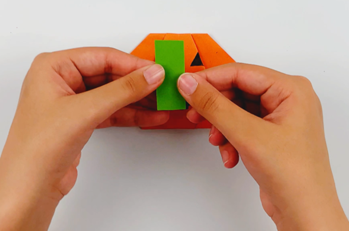 Two hands cutting a small rectangular piece of green paper for the pumpkin stalk.