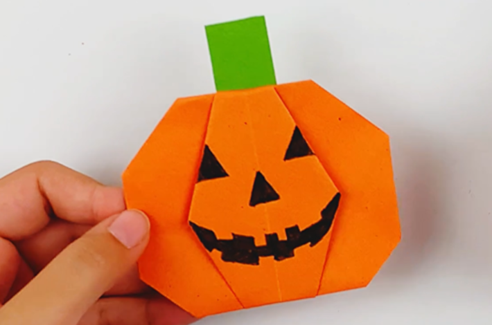 A hand holding the pumpkin with the stalk glued to the back of it. 