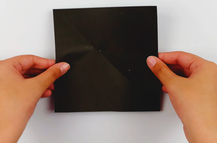 Two hands holding a black square piece of paper. 