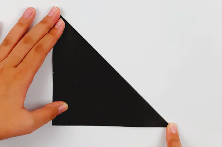 Two hands folding the top right corner of the paper to the bottom left to form a triangle. 