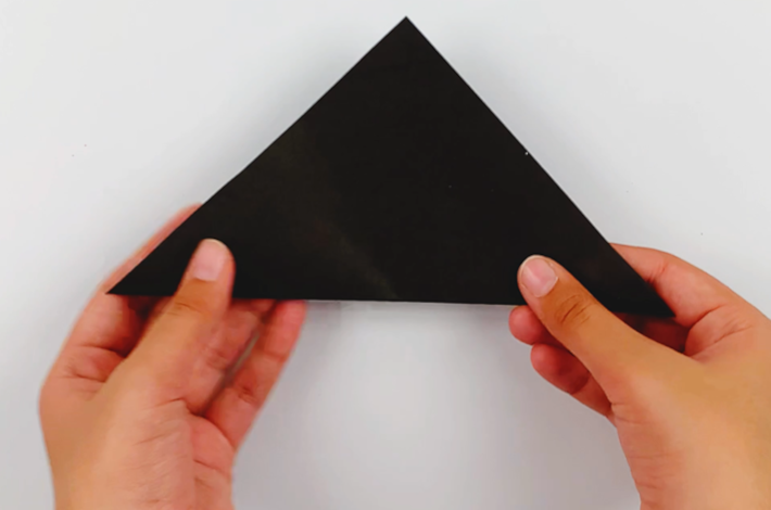 Two hands holding the triangle of black paper so the longest edge is on the bottom.