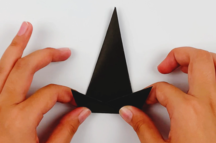 Two hands folding the bottom section of the black paper upwards. 