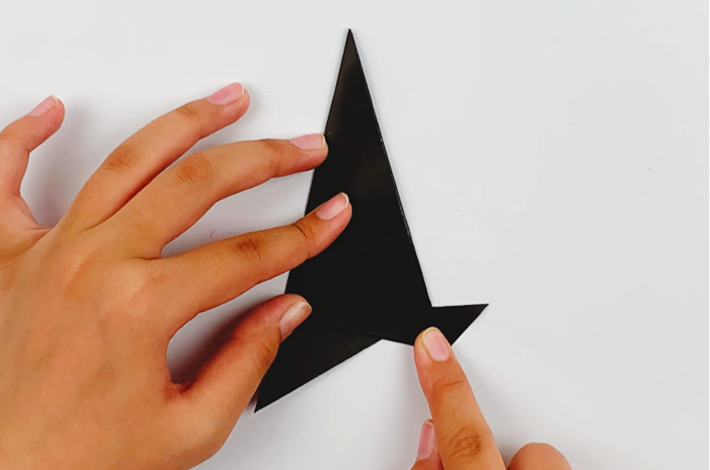 Two hands folding the bottom right-hand point up and over to form a straight line for the hat brim.