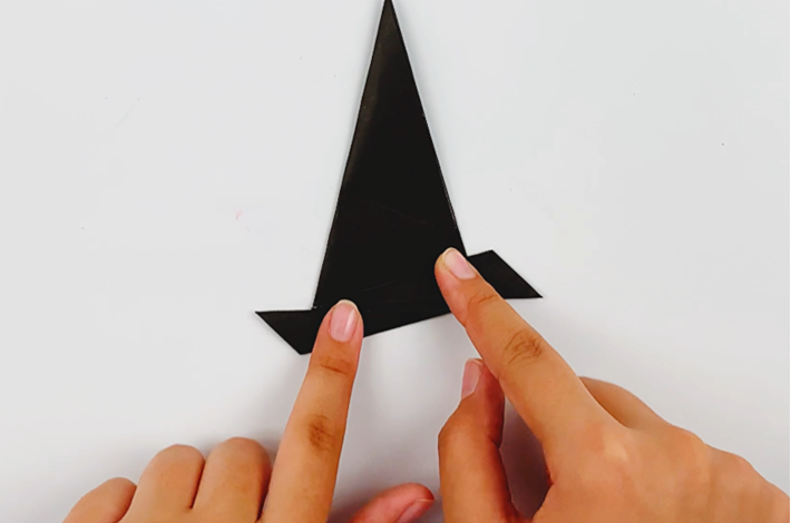 Two hands folding the bottom left-hand point up and over to form a straight line for the hat brim.