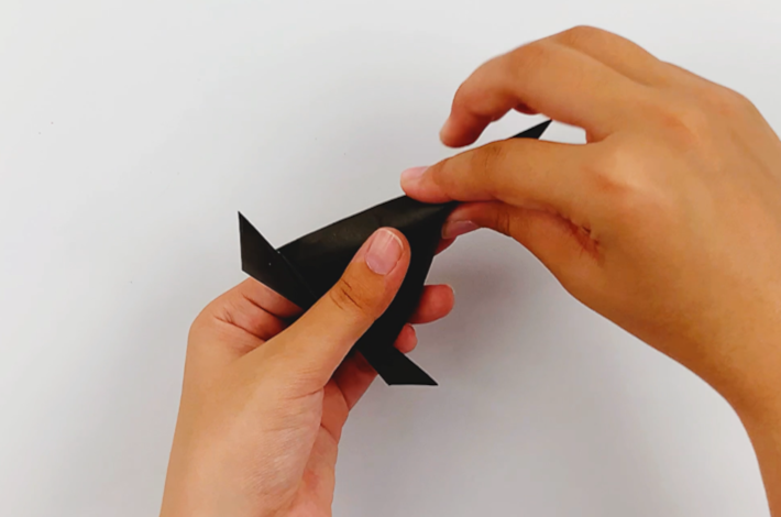 Two hands crinkling the paper at the top of the hat and twirling it to give a worn look and feel. 