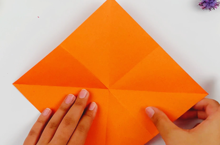 Two hands opening up the square piece of paper to show the fold lines. 