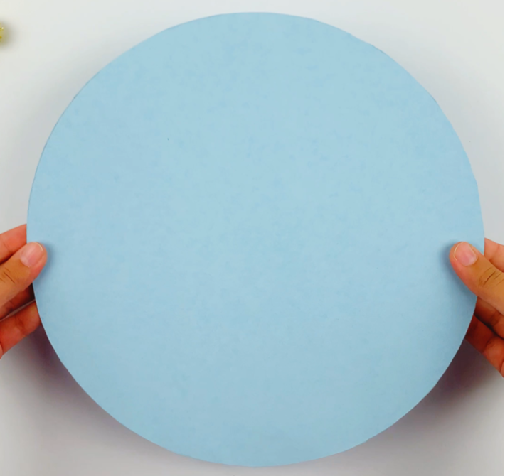 Two hands holding a blue circle cut from colored paper. 