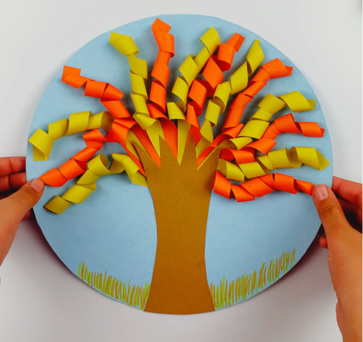 Two hands holding a completed paper craft fall tree. 