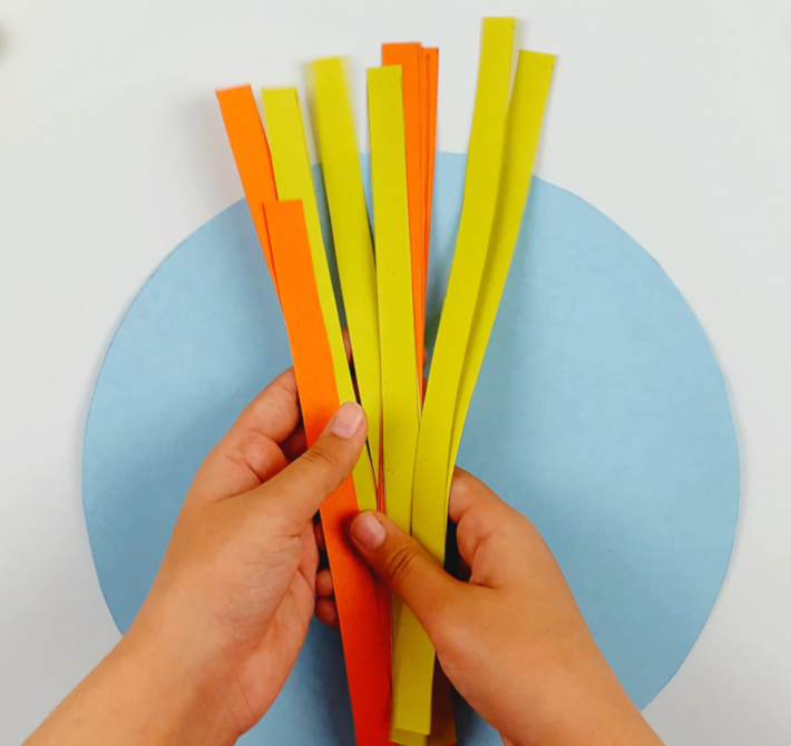 Two hands holding yellow and orange paper strips.