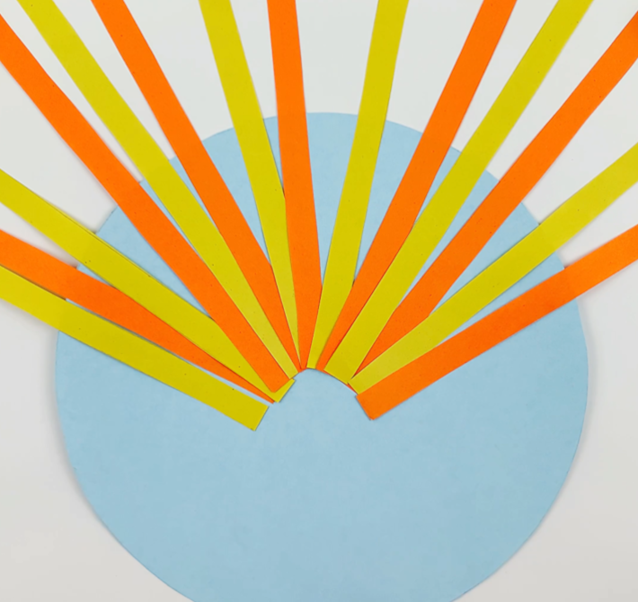 A blue paper circle with the orange and yellow paper strips glued onto it.