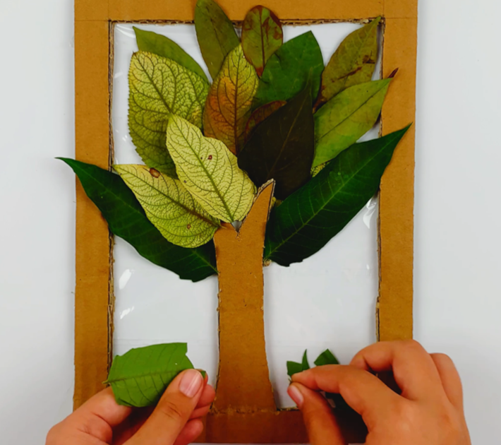 Two hands adding smaller pieces of leaf to the bottom of the frame. 