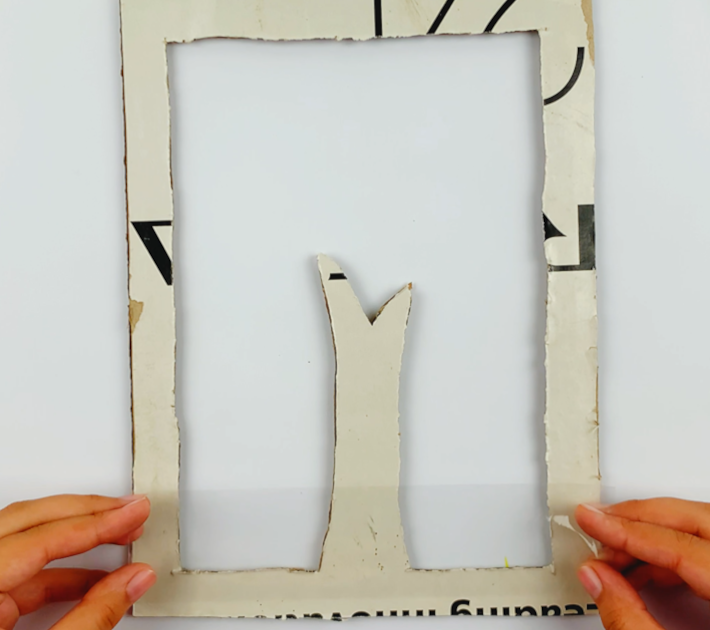 Two hands sticking a piece of Scotch tape to the bottom of the frame, which has been flipped over. 