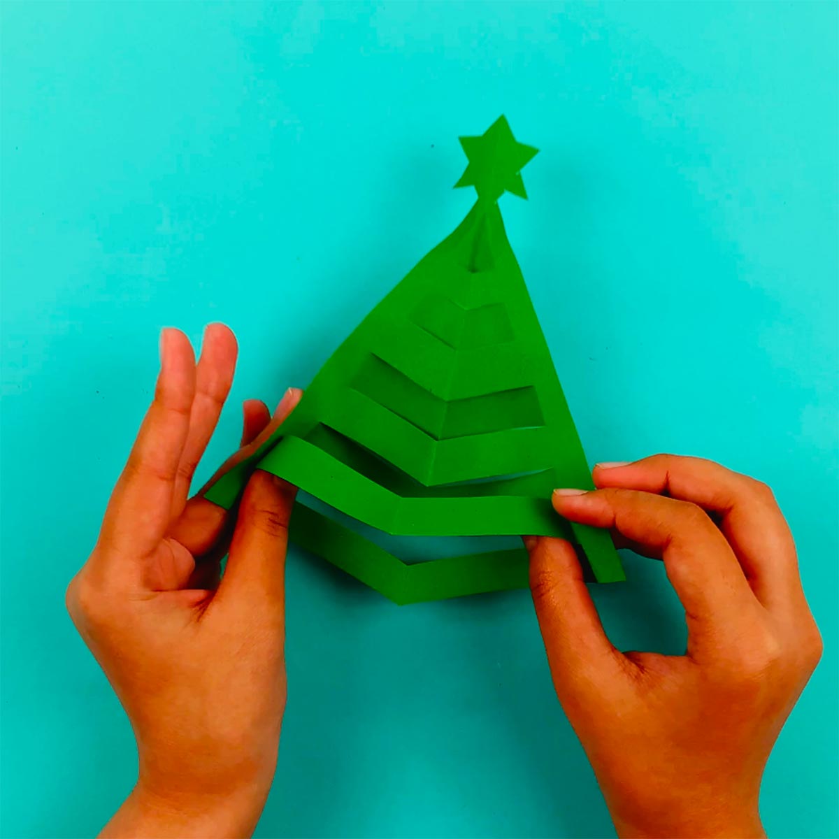 Two hands manipulating the third, fifth, and seventh sections of cut paper to make it stand out with a 3d effect.