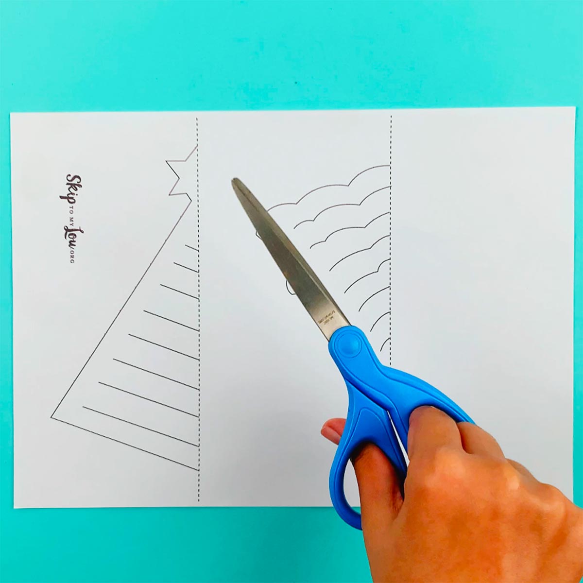 A hand holding a pair of scissors over the 3D paper tree templates.