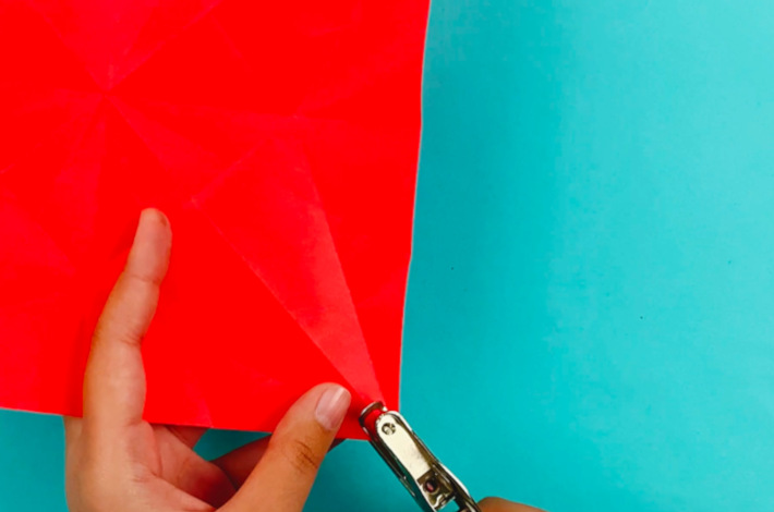 Two hands using a punch to make a hole in each of the four points.