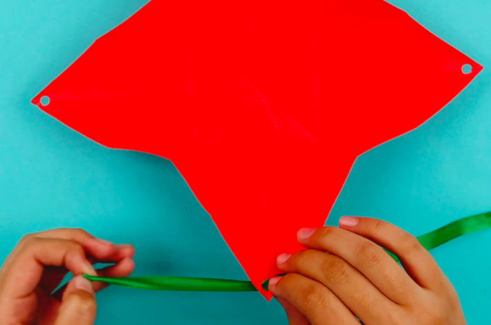 Two hands threading a green ribbon through the holes that have been punched.