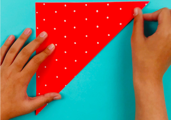 Two hands folding the decorative paper into a triangle after flipping it over.