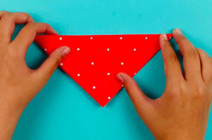 Two hands folding the larger triangle into a smaller one from the bottom to the top.