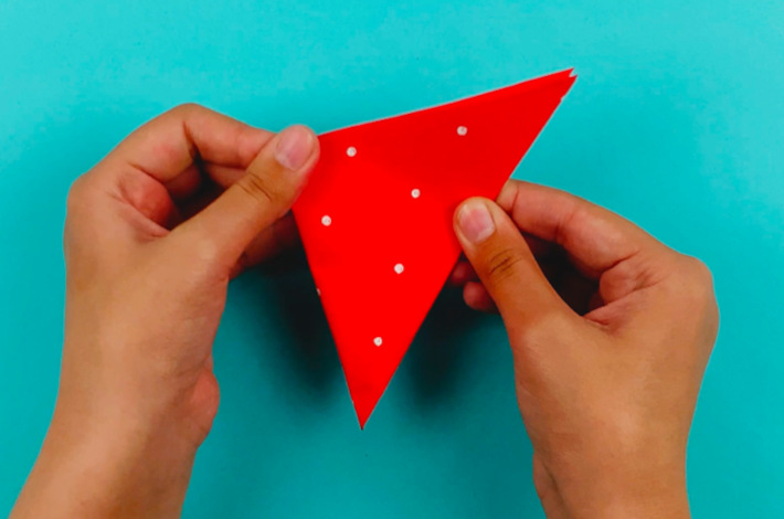 Two hands folding the bigger triangle into a smaller one by folding the paper from left to right.